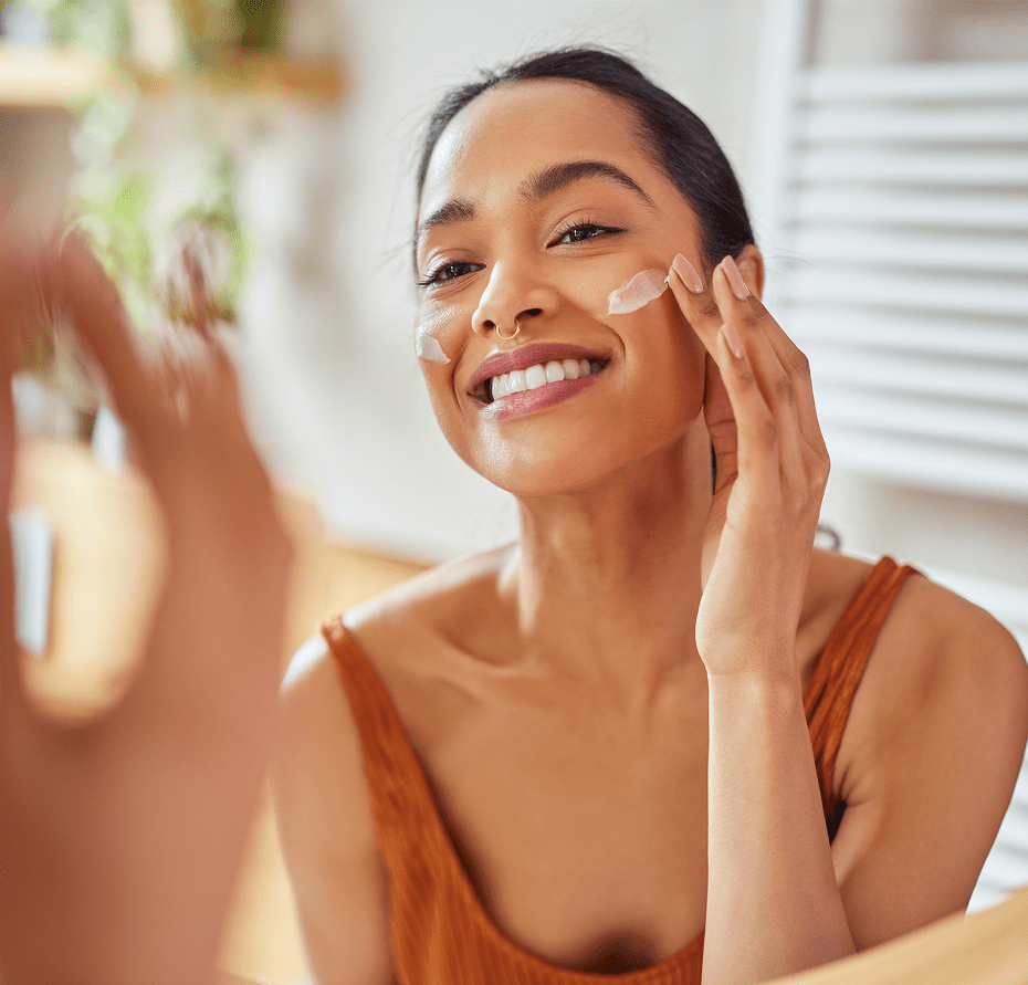 Woman applying moisturizer in front of mirror.